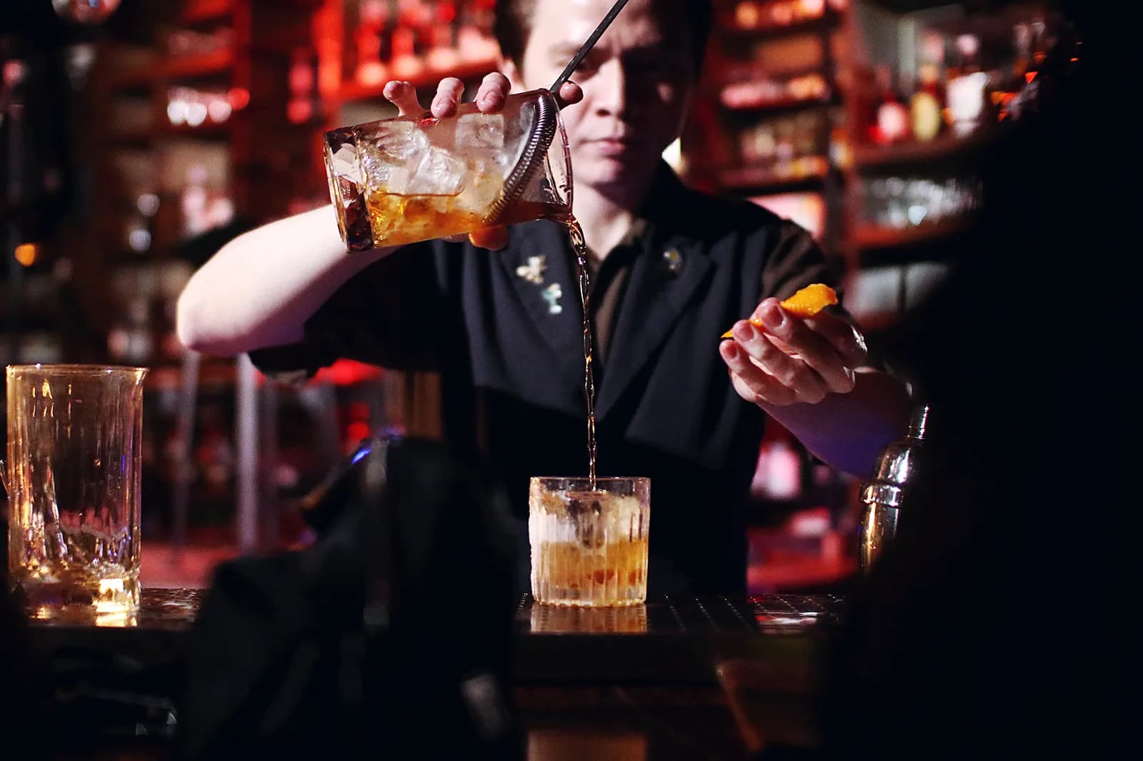 A pale cocktail beside books and spirits on the dimly lit bar.