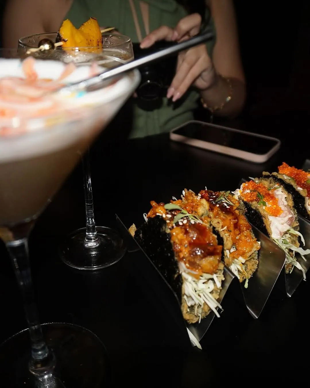 A cocktail beside a plate of sushi rolls at the bar.