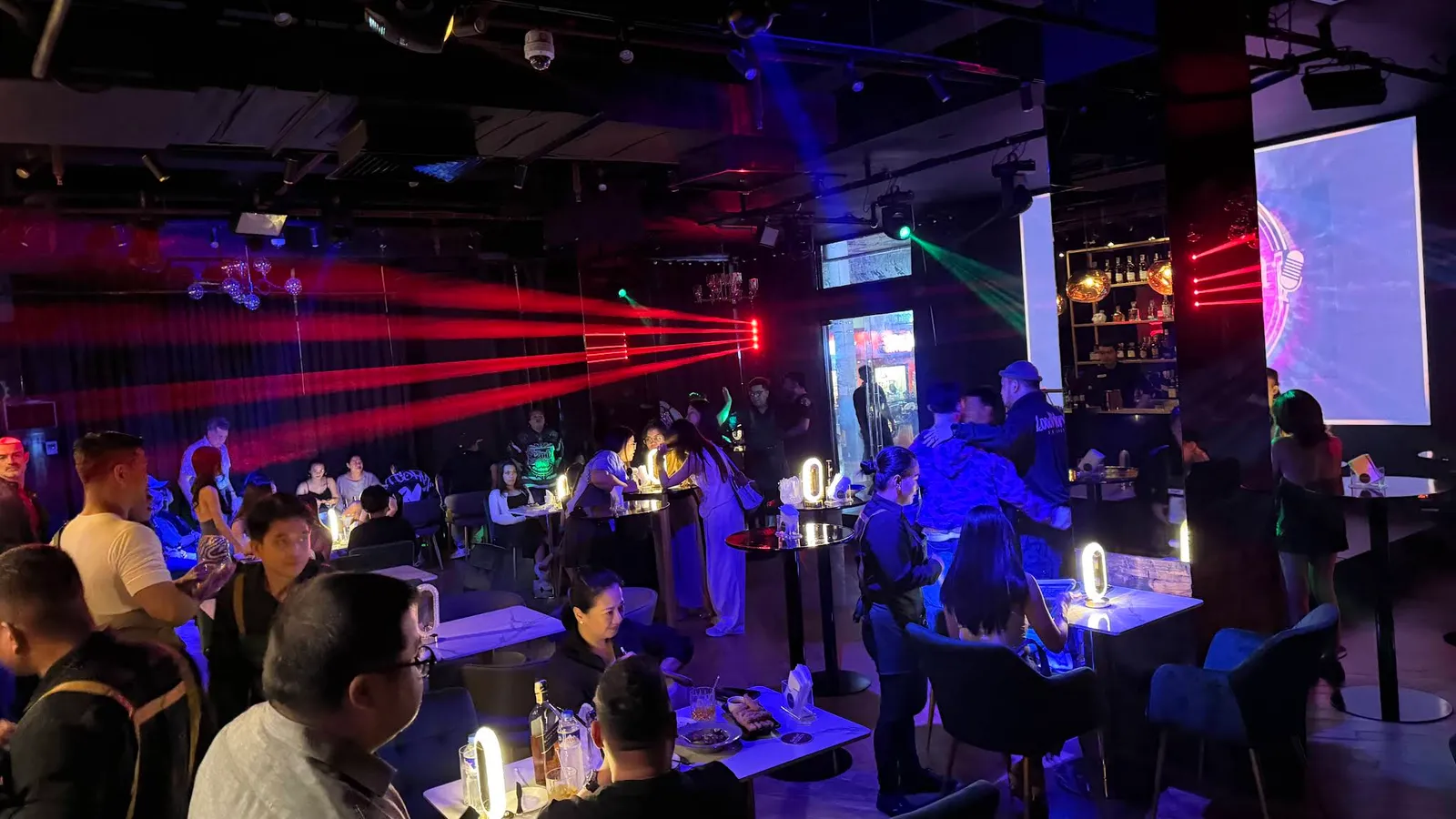 Blue- and red-lit bar interior with guests seated around tables at night