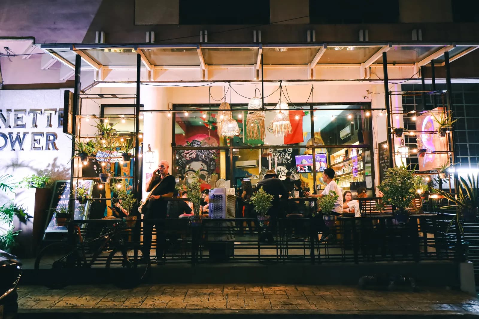 Open-front bar glowing at night with tables, plants and guests inside