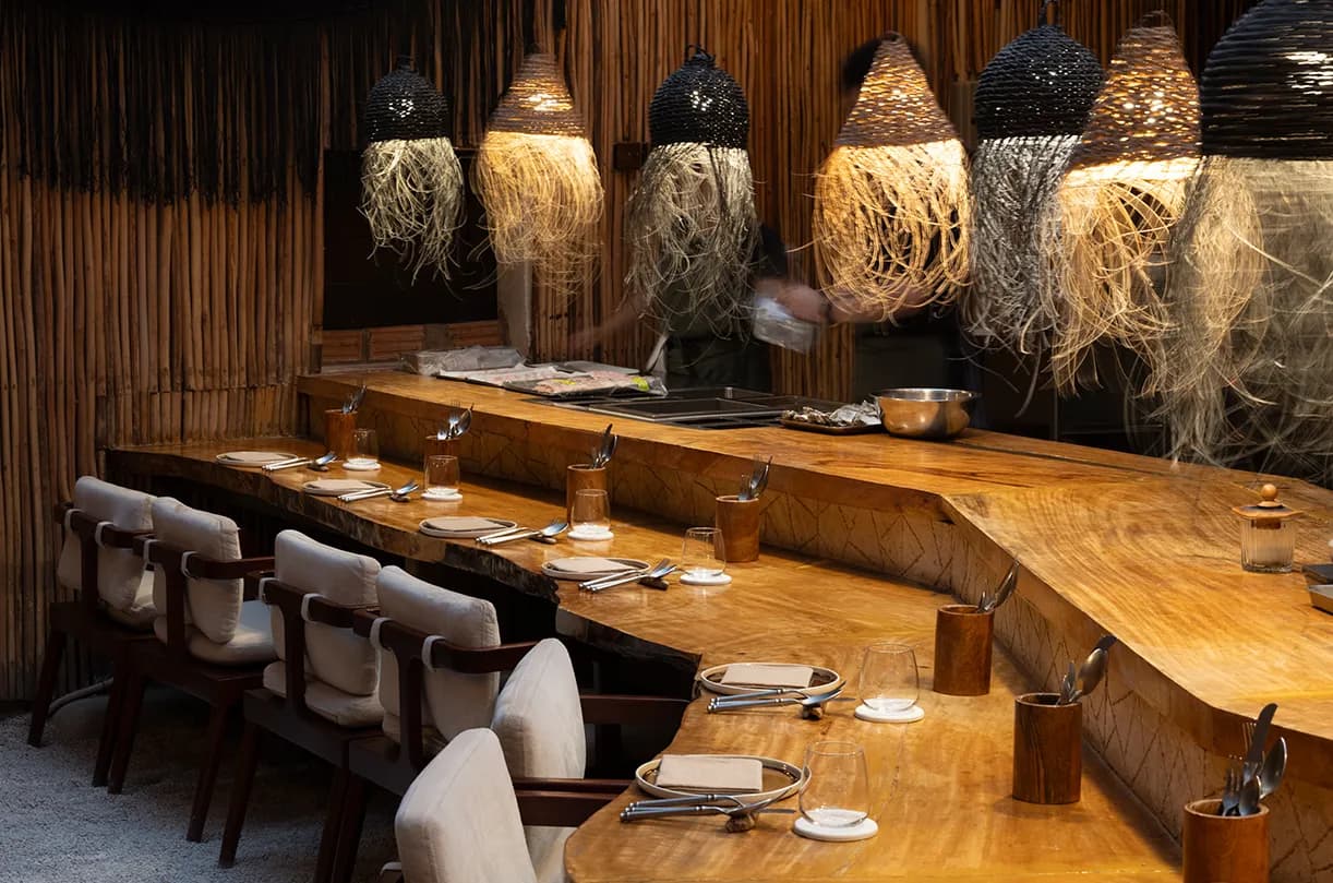 Firewood kitchen counter set for dinner beneath woven pendant lights.