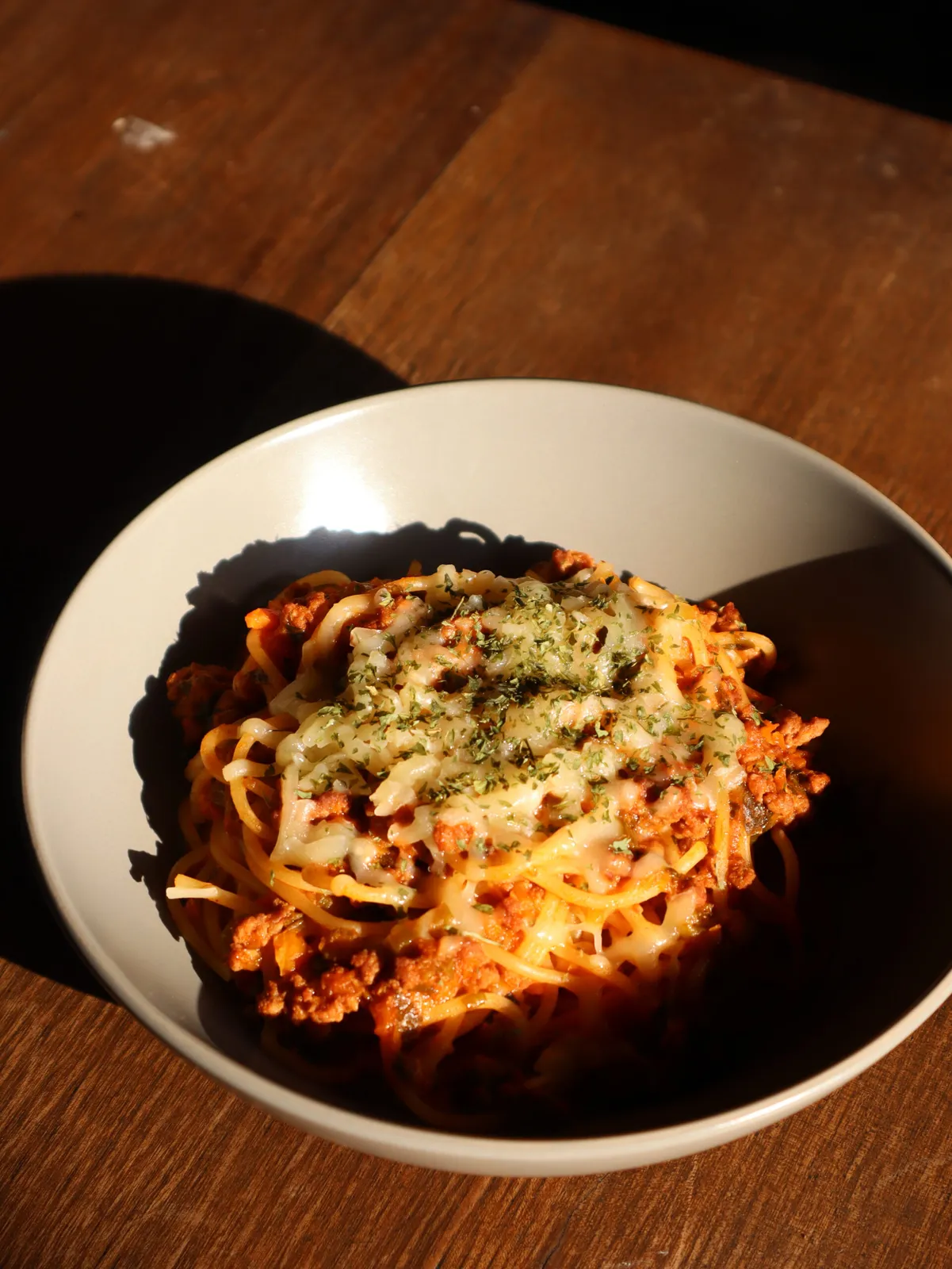 A bowl of spaghetti with meat sauce and melted cheese.