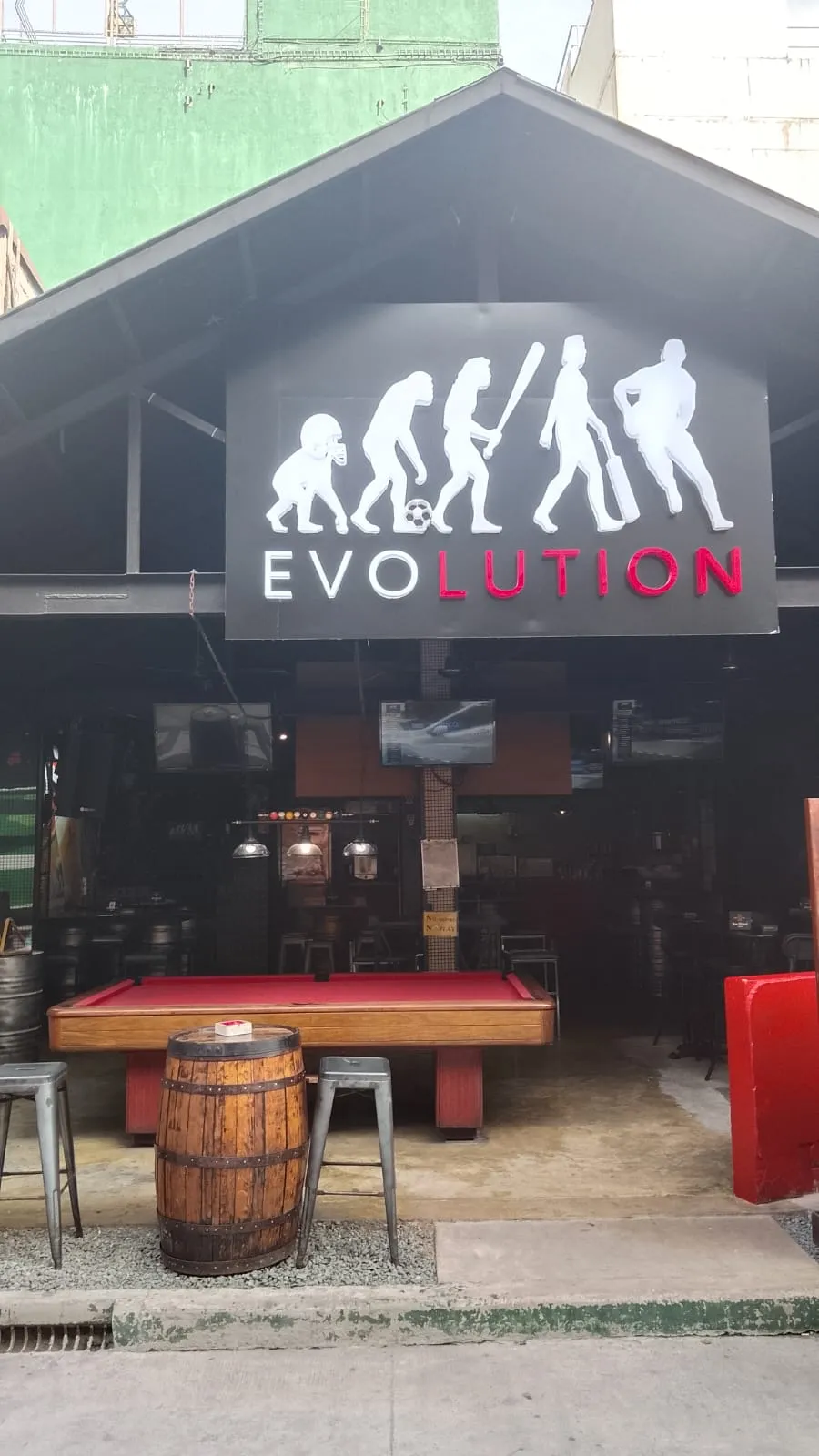 Daytime view of Evolution's open frontage with a red pool table and barrel tables
